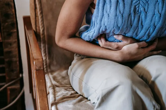 Seated woman holding a knitted hot-water bottle against her lower abdomen, face out of frame