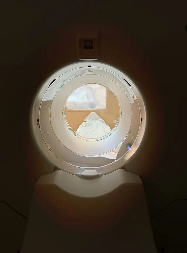 View through the bore of a CT scanner toward the empty patient table, lit softly against a dark surround