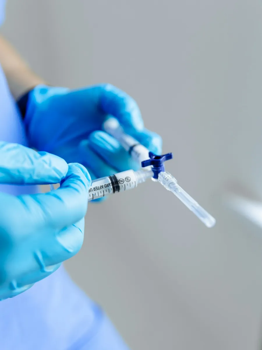 Gloved hands joining two syringes with a three-way tap, the set-up used to mix sclerotherapy foam