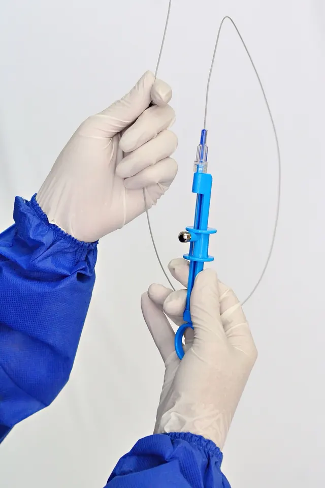 Gloved hands in a blue sterile gown holding a looped guidewire with a blue torque device