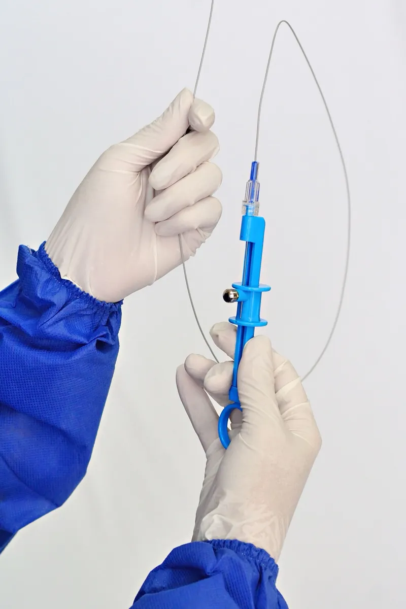 Gloved hands in a blue sterile gown holding a looped guidewire with a blue torque device