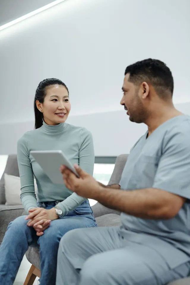 Smiling Asian woman listening to a clinician in scrubs who is explaining something on a tablet
