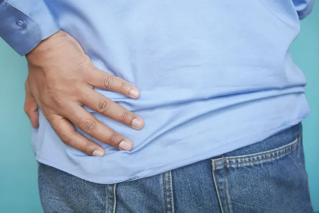 Close-up of a hand pressed to the side of the lower back over a light blue shirt and jeans