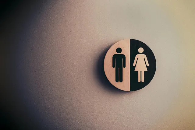 Round wooden toilet sign with male and female figures on a softly lit wall