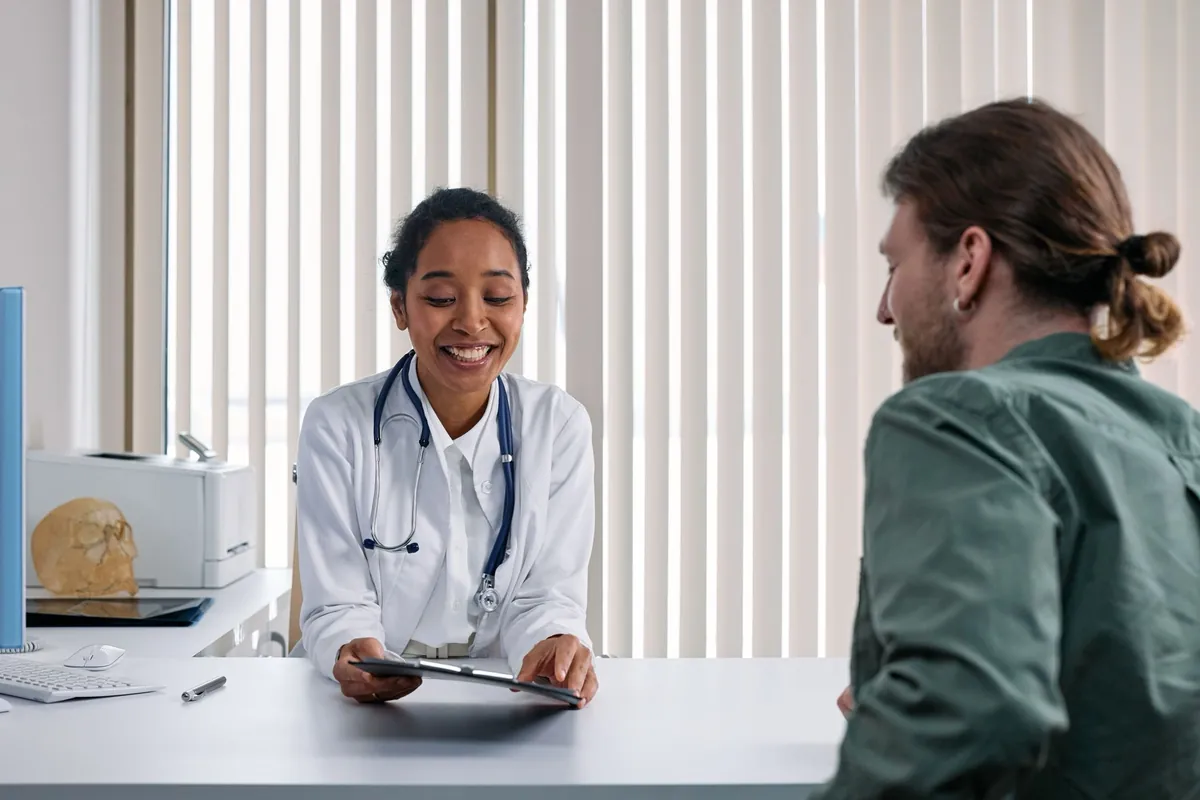 Doctor in a white coat talking with a young man across a desk in a bright clinic office