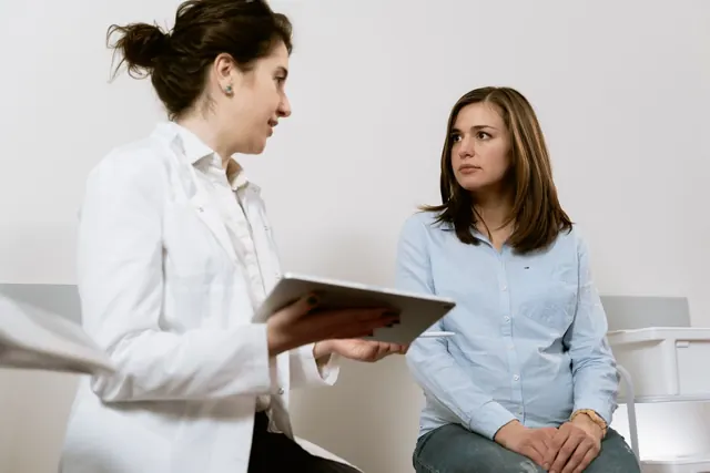 Female doctor holding a tablet explains results to a seated woman in an examination room