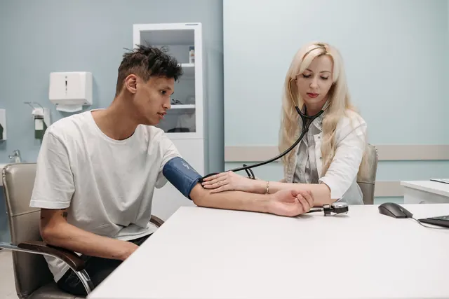 Young man in a white T-shirt having his blood pressure checked by a female doctor at a clinic desk