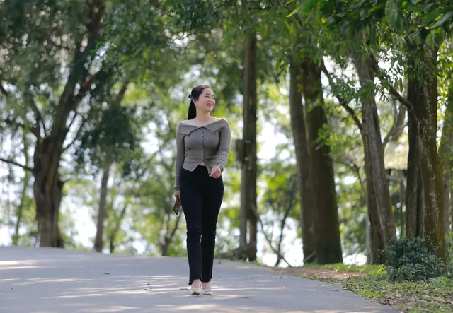 Smiling Asian woman walking along a tree-lined park path